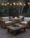 Rustic deck featuring reclaimed wood decking, a rough-hewn teak coffee table, and woven rattan armchairs with natural linen cushions. Edison bulb string lights are draped overhead, casting a warm glow, complemented by a stone fire pit in the background. — view 3