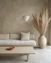 A minimalist Japandi living room featuring a low-profile sofa in natural linen, a light ash wood coffee table, and a large, unglazed ceramic vase with dried pampas grass. The walls are painted in a warm grey, complemented by soft, diffused light from a paper-shade floor lamp. — view 2