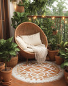 A bohemian exterior balcony featuring a terracotta floor, a woven outdoor rug with a geometric pattern, and a rattan egg chair adorned with cream cushions and a macrame throw. Lush green potted plants in various terracotta and woven planters are arranged around, with warm string lights draped overhead. — view 3