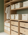 A Japandi-style closet featuring light ash wood shelving and drawers, cream linen storage boxes, and a subtle sage green accent wall, bathed in soft, natural light. — view 4