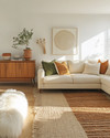 A bohemian great room blending vintage and modern elements, featuring a cream sectional sofa, a mid-century teak credenza, layered jute and sheepskin rugs, and a mix of terracotta and sage green accents. — view 4