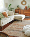 A bohemian great room blending vintage and modern elements, featuring a cream sectional sofa, a mid-century teak credenza, layered jute and sheepskin rugs, and a mix of terracotta and sage green accents. — view 3