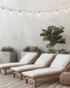A minimalist boho deck featuring light teak wood lounge chairs with off-white cushions, subtle woven rattan accents, and large concrete planters holding a Fiddle-Leaf Fig and various succulents, all under warm string lights. — close-up of textures and materials