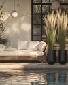 A Scandinavian poolside area featuring a large reclaimed teak daybed with cream linen cushions, oversized woven rattan armchairs, and matte black metal planters with tall Horsetail Reed plants, all under the soft glow of spherical outdoor lanterns. — alternate angle