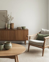 A Scandinavian Craft living room blending vintage and modern, featuring a light oak coffee table, a mid-century teak sideboard, a contemporary sofa in a light grey linen, and a woven rattan armchair, accented with handmade pottery and muted green textiles. — styling and décor detail