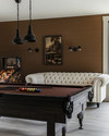Farmhouse game room with a dark wood billiard table, a cream linen Chesterfield sofa, matte black metal lighting fixtures, and a vintage pinball machine against a wall painted in 'Swiss Coffee'. — close-up of textures and materials