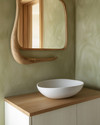 A serene Japandi powder room featuring a floating white oak vanity with a matte white vessel sink, an organically shaped mirror with a slim natural wood frame, and a soft sage green limewash wall.