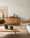 A Scandinavian Craft living room blending vintage and modern, featuring a light oak coffee table, a mid-century teak sideboard, a contemporary sofa in a light grey linen, and a woven rattan armchair, accented with handmade pottery and muted green textiles. — close-up of textures and materials