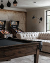 Farmhouse game room with a dark wood billiard table, a cream linen Chesterfield sofa, matte black metal lighting fixtures, and a vintage pinball machine against a wall painted in 'Swiss Coffee'. — styling and décor detail
