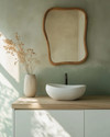 A serene Japandi powder room featuring a floating white oak vanity with a matte white vessel sink, an organically shaped mirror with a slim natural wood frame, and a soft sage green limewash wall. — close-up of textures and materials