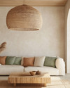 A boho poolhouse interior with a large woven rattan pendant light, a cream sofa with textured cushions, and a natural wood coffee table. Soft, diffused lighting creates a serene atmosphere, complemented by muted terracotta and sage green accents. — styling and décor detail