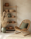 A calm boho garage interior with warm off-white walls, light oak shelving, a natural rattan chair, and muted sage green and terracotta accents in ceramic planters, all bathed in soft, warm light.