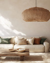 A boho poolhouse interior with a large woven rattan pendant light, a cream sofa with textured cushions, and a natural wood coffee table. Soft, diffused lighting creates a serene atmosphere, complemented by muted terracotta and sage green accents. — alternate angle