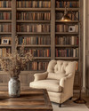 Farmhouse library with a large built-in bookshelf filled with books, a comfortable armchair upholstered in a warm beige fabric, and a weathered wood coffee table adorned with a vase of dried flowers, all under the soft glow of a bronze-finished floor lamp. — alternate angle