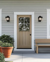 A serene Scandinavian exterior with a light gray facade, crisp white trim, and a natural wood front door. Simple black sconces flank the door, and a minimalist wooden bench sits beside terracotta planters filled with green foliage, all under a bright, clear sky. — styling and décor detail
