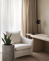 A serene Japandi home office with a pale oak desk, a minimalist matte black desk lamp, and an off-white linen armchair. Natural light streams through sheer curtains, illuminating a small snake plant in a raw concrete planter. — alternate angle