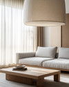 A Japandi family room showcasing a large, linen-shaded drum pendant light, a low-profile light grey sofa, and a minimalist oak coffee table, with soft daylight filtering through sheer curtains. — alternate angle