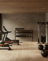 A clean rustic home gym featuring light reclaimed wood flooring, a smooth concrete accent wall, a simple black wrought iron shelf, and minimalist workout equipment with wooden and leather details, bathed in soft ambient lighting. — close-up of textures and materials