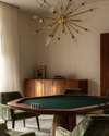 A mid-century modern game room featuring a walnut poker table with a dark green felt top, surrounded by olive velvet low-slung armchairs, illuminated by a brass Sputnik chandelier, with a teak credenza against a soft ivory wall. — close-up of textures and materials