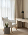 A serene Japandi home office with a pale oak desk, a minimalist matte black desk lamp, and an off-white linen armchair. Natural light streams through sheer curtains, illuminating a small snake plant in a raw concrete planter. — close-up of textures and materials