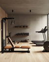 A clean rustic home gym featuring light reclaimed wood flooring, a smooth concrete accent wall, a simple black wrought iron shelf, and minimalist workout equipment with wooden and leather details, bathed in soft ambient lighting. — styling and décor detail