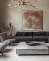 Modern great room featuring a low-profile charcoal grey sectional sofa, a large polished concrete coffee table, and a pair of bouclé accent chairs. A dramatic brushed brass chandelier hangs above, complemented by a large abstract painting on a light greige wall. — close-up of textures and materials