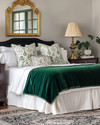A traditional bedroom featuring a bed dressed in white and cream sateen bedding, layered with a deep emerald green velvet throw and patterned decorative pillows. A large ornate gold-framed mirror hangs above a dark wood dresser, flanked by classic brass table lamps with pleated fabric shades. A muted Persian-style rug covers the floor. — close-up of textures and materials