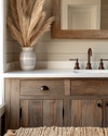 A cozy rustic powder room featuring a reclaimed wood vanity with an off-white quartz countertop, an oil-rubbed bronze faucet, and shiplap walls painted in a soft greige. A woven jute rug sits on the floor, and a ceramic vase with dried pampas grass adorns the counter. — close-up of textures and materials