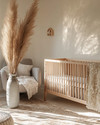 A serene Japandi baby room with a light wood crib, a soft grey glider, and a neutral rug, accented by a tall dried pampas grass arrangement in a ceramic vase and a subtly patterned throw blanket. — styling and décor detail