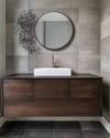 A modern powder room features a floating dark wood vanity with an integrated white quartz sink and brushed nickel faucet, set against large format charcoal grey porcelain tiles. A simple round mirror and abstract metal wall art complete the sleek, resilient design. — close-up of textures and materials