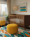 A vibrant Mid-Century Modern baby's room in a small apartment, featuring a natural wood convertible crib, a mustard yellow storage ottoman, and a geometric area rug with teal and orange accents. — close-up of textures and materials