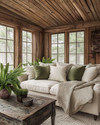 A rustic sunroom featuring a natural wood ceiling, a comfortable sofa with cream linen cushions, a chunky knit throw, and sage green accent pillows, surrounded by potted ferns and a vintage distressed wooden coffee table. — styling and décor detail