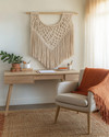 A cozy boho home office with a light wood desk, a macramé wall hanging, and a comfortable armchair, featuring a jute rug and a vibrant terracotta throw, designed for family and pet-friendly living. — styling and décor detail