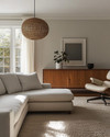 A Mid-Century Modern Craft living room featuring a walnut credenza, a low-slung sofa in natural linen, an Eames Lounge Chair, and a woven rattan pendant light, all bathed in warm, natural light. — close-up of textures and materials