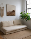 A small Boho Landscape living room featuring a low-slung sofa in natural linen, layered jute rugs, a minimalist abstract desert landscape print on the wall, and a trailing Pothos plant in a macrame hanger near a window.