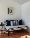 A compact traditional poolhouse interior featuring white beadboard walls, a small daybed with navy and white striped cushions, a wrought iron side table, and terracotta tile flooring, bathed in natural light. — close-up of textures and materials