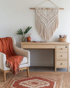 A cozy boho home office with a light wood desk, a macramé wall hanging, and a comfortable armchair, featuring a jute rug and a vibrant terracotta throw, designed for family and pet-friendly living. — alternate angle