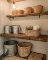 Rustic laundry room with a reclaimed wood floating shelf, galvanized metal buckets, woven rattan baskets, and a small braided jute rug on the floor, lit by a warm Edison bulb pendant. — alternate angle