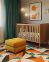 A vibrant Mid-Century Modern baby's room in a small apartment, featuring a natural wood convertible crib, a mustard yellow storage ottoman, and a geometric area rug with teal and orange accents. — styling and décor detail