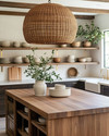 A bohemian kitchen featuring a large woven rattan pendant light above a wooden island with fresh greenery, open shelving with ceramic dishes, and warm brass fixtures creating a cozy, inviting ambiance. — alternate angle