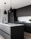 A sleek modern kitchen featuring matte black handleless cabinetry, white quartz countertops, integrated stainless steel appliances, and a minimalist black pendant light over a large kitchen island. — styling and décor detail