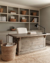 A warm farmhouse home office featuring a large distressed oak desk, a cream linen office chair, open shelving with books and woven baskets, and walls painted in a soft greige. A braided jute rug grounds the space, and a matte black task lamp sits on the desk. — close-up of textures and materials