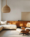 A Mid-Century Modern Craft living room featuring a walnut credenza, a low-slung sofa in natural linen, an Eames Lounge Chair, and a woven rattan pendant light, all bathed in warm, natural light. — alternate angle
