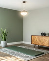 Mid-Century Modern home gym with a muted olive green accent wall, light gray walls, a Sputnik-style pendant light, and a teak-veneered credenza. A yoga mat is laid out on a geometric wool rug, with a snake plant in a ceramic planter. — styling and décor detail