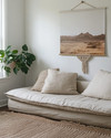 A small Boho Landscape living room featuring a low-slung sofa in natural linen, layered jute rugs, a minimalist abstract desert landscape print on the wall, and a trailing Pothos plant in a macrame hanger near a window. — close-up of textures and materials