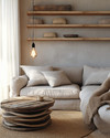 A cozy rustic living room in an apartment setting, featuring a compact linen sofa, a reclaimed wood nesting coffee table, and open shelving made from rough-hewn timber. Natural light filters through the window, illuminating jute rugs and woven wool throws, complemented by a simple pendant light with an Edison bulb. — alternate angle