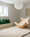 A bright Scandinavian basement living area featuring a light oak sculptural lounge chair, a large cream hand-knotted wool rug, and an oversized white paper lantern pendant light, with subtle forest green textile accents. — close-up of textures and materials