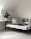 A bright Scandinavian garage loft with white walls, pale oak flooring, and a minimalist black metal frame daybed, accented with a light grey throw and a simple potted snake plant on a white floating shelf. — styling and décor detail