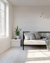 A bright Scandinavian garage loft with white walls, pale oak flooring, and a minimalist black metal frame daybed, accented with a light grey throw and a simple potted snake plant on a white floating shelf. — alternate angle