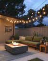 A cozy Mid-Century Modern backyard featuring a low-profile sectional with olive green cushions, a sleek concrete fire pit, and warm string lights draped overhead, complemented by teak side tables and potted snake plants. — close-up of textures and materials
